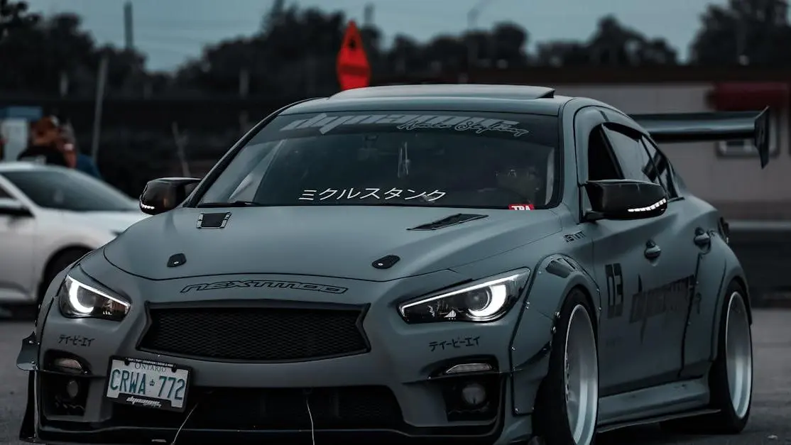 Grey sports car with custom decals and newly installed hood scoop outdoors.