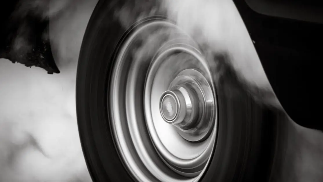 Spinning car wheel emitting smoke, illustrating ideal tire pressure for drag racing.