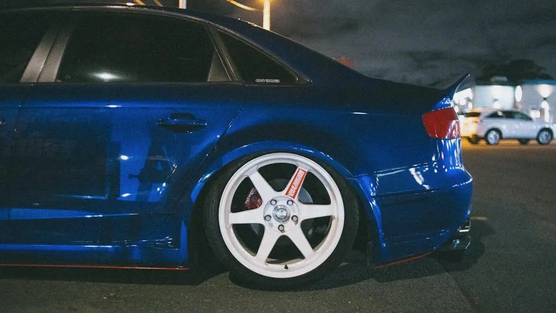 Blue luxury car with aftermarket automobile wheels parked at night, showcasing custom rims and sleek style.