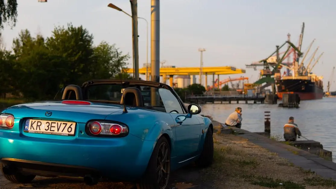 Blue Mazda MX‑5 Miata with body kit by Gdańsk harbor, people enjoying waterfront view