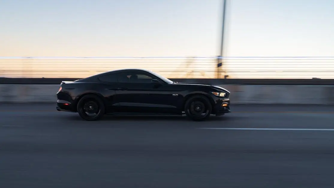 Sleek black car at dusk on a bridge, showcasing aerodynamic styling, motion, and speed