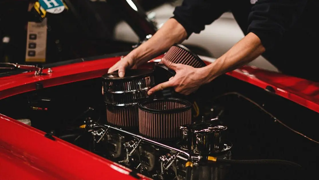 Mechanic installing air filters on classic red car engine, showcasing aftermarket auto industry