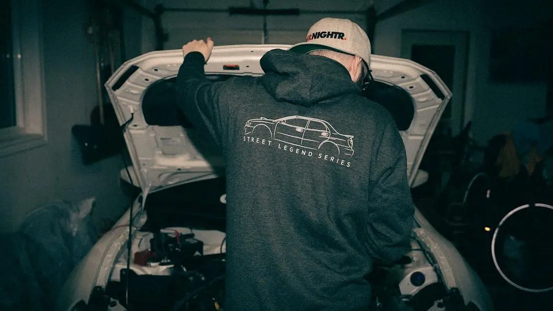 Mechanic in hoodie tuning car engine at night garage, Street Legend Series—automotive aftermarket industry