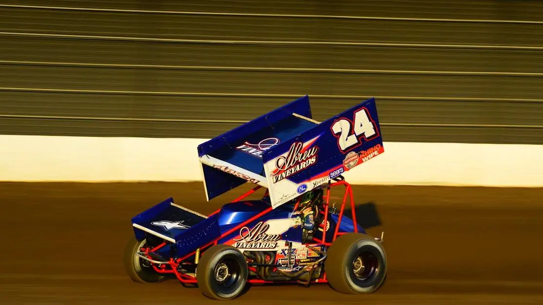 Blue micro sprint car racing on a dirt track, kicking up dust and showcasing speed and excitement.