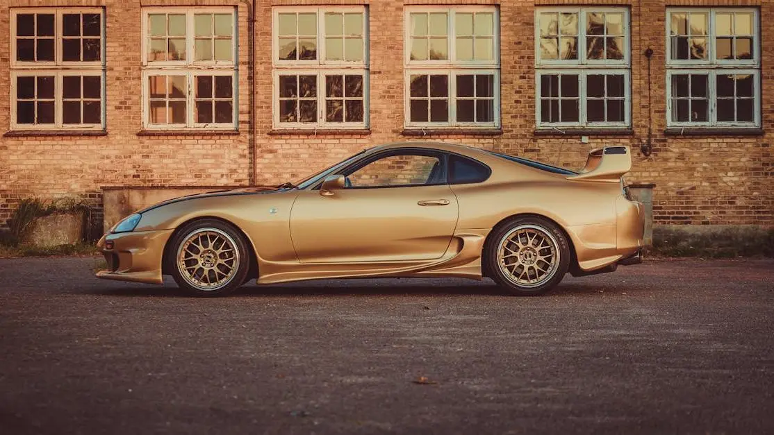 RX7 body kit FC in gold parked before vintage industrial brick building cover photo