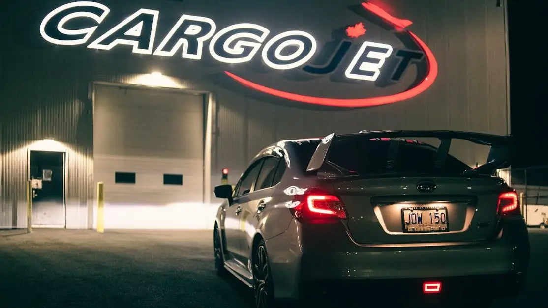 Silver Subaru BRZ spoiler kit parked at night before illuminated CargoJet sign